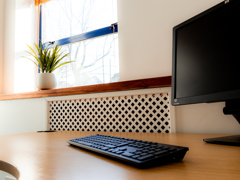 A computer monitor and keyboard on a wooden desk near a window with a potted plant. Sunlight shines through the window, creating a bright and clean workspace atmosphere—an ideal setting for any serviced office or meeting room in Glasgow.