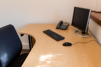 A wooden desk with a computer monitor, keyboard, mouse, office phone, and a black chair in a bright, clean Caledonia Business Centre office space.